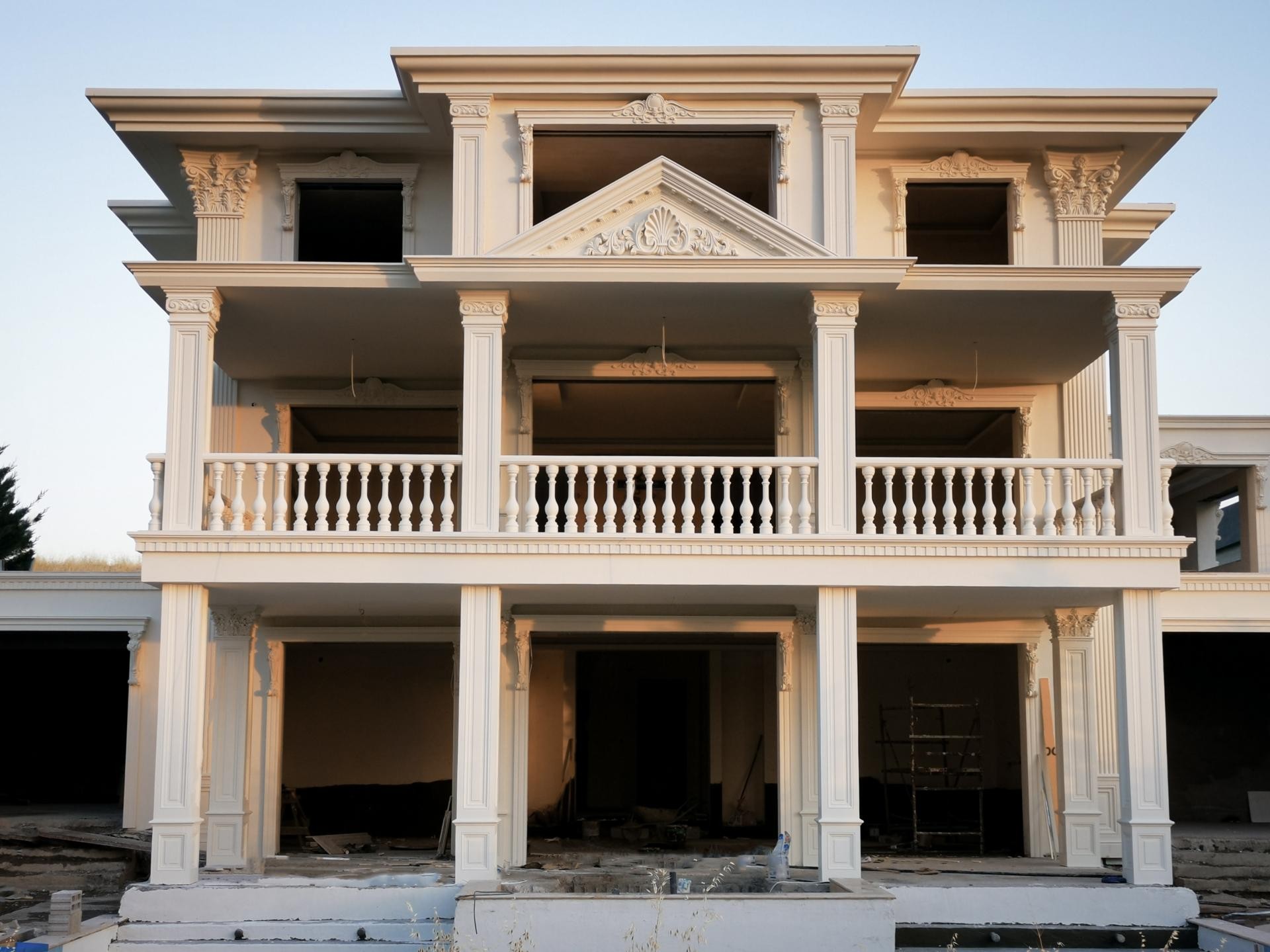 Üç katlı açık renkli bir villanın dış cephesinde kullanılmış beyaz poliüretan pilaster sütunlar, pencere söveleri ve klasik pediment taç detayları.