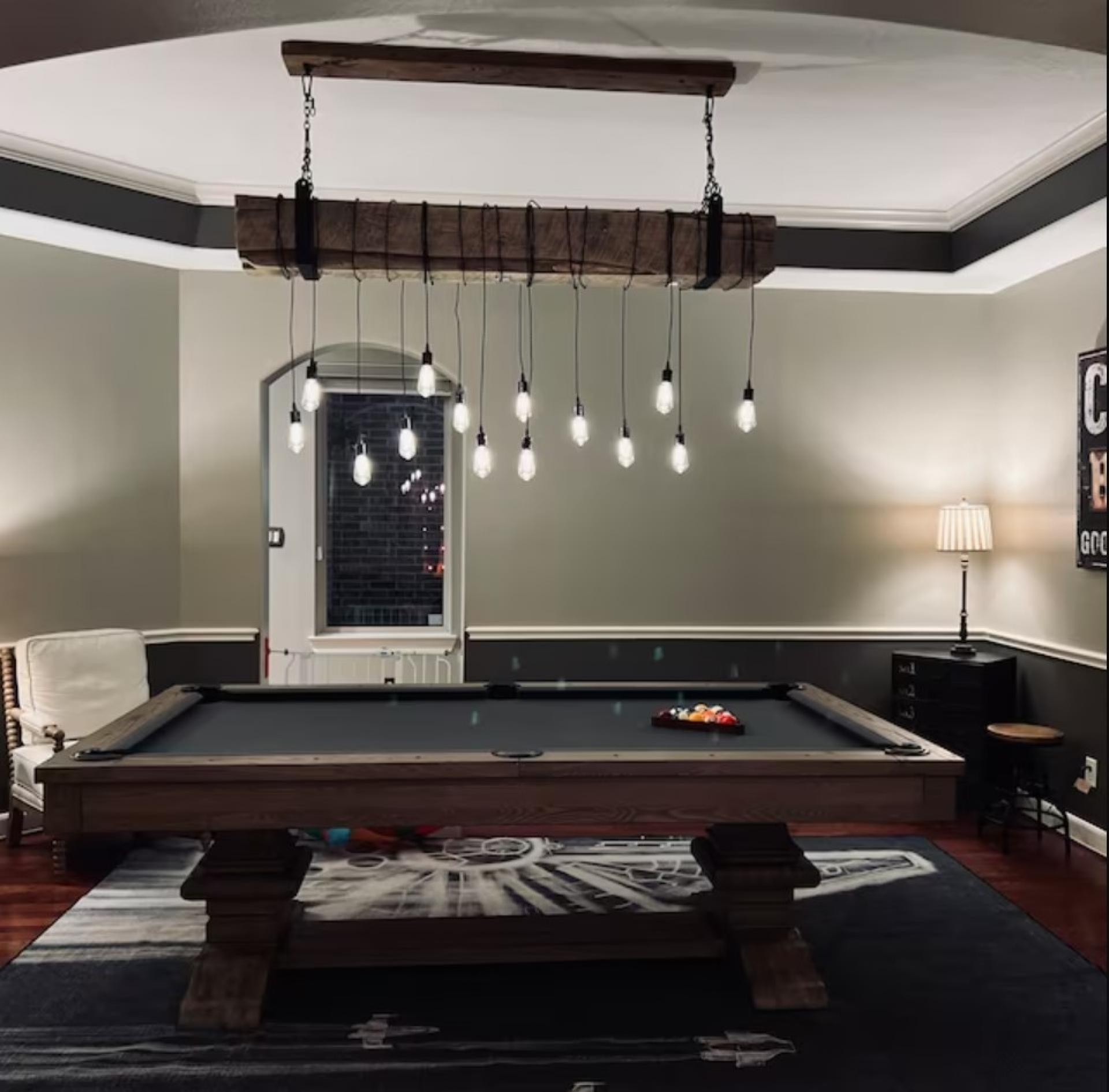 Ortamdaki bilardo masasının üzerinde odak noktası oluşturan, koyu kahverengi rustik kütüğe sarılı sarkıt ampuller içeren tavan aydınlatması.