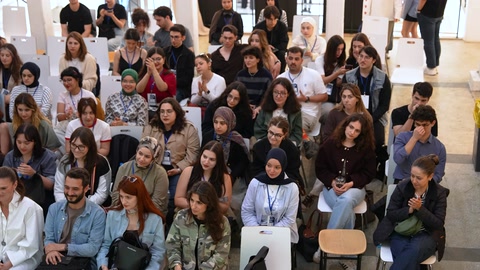 Kalabalık öğrenci grubu basamaklı oturma alanından sunumu izliyor