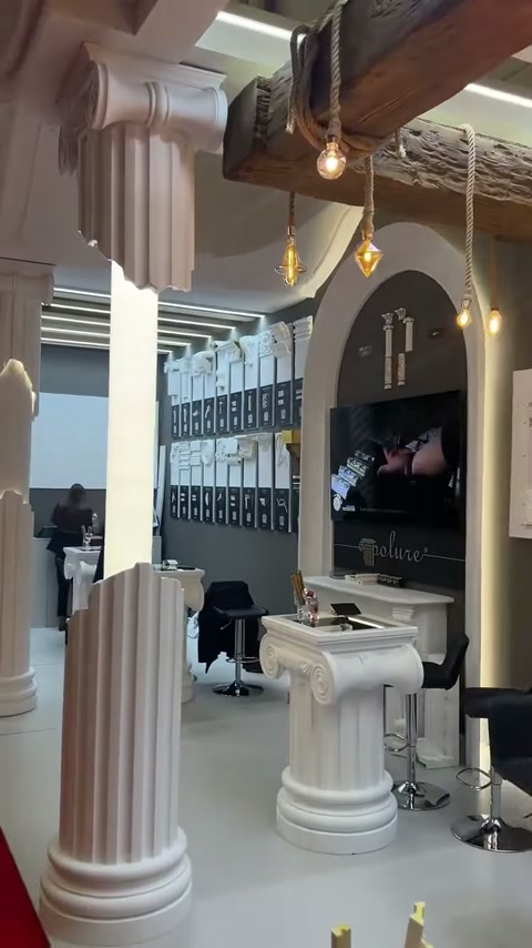 Yivli sütunlar, ahşap tavan kirişleri ve sarkıt lambalar standı çevreliyor
