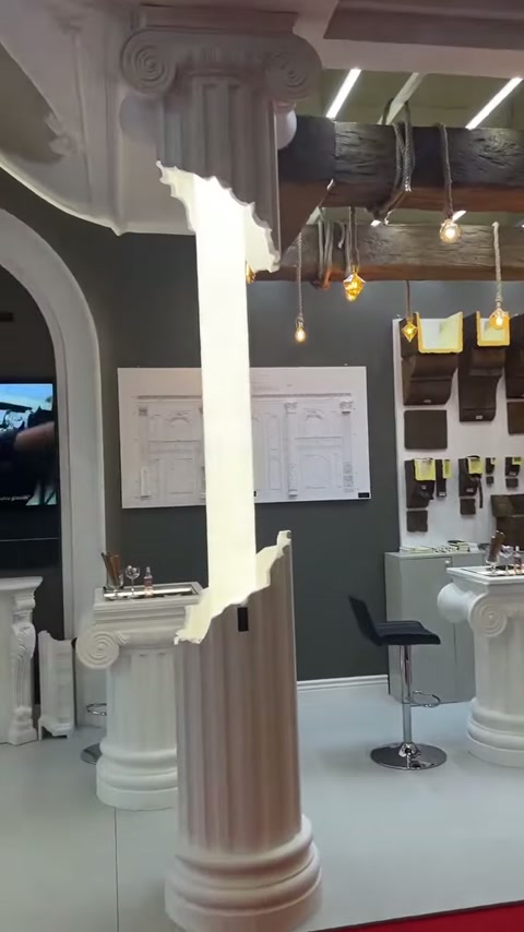 Antik sütun başlığı ve yivli gövde, standın dekoratif girişini çerçeveliyor