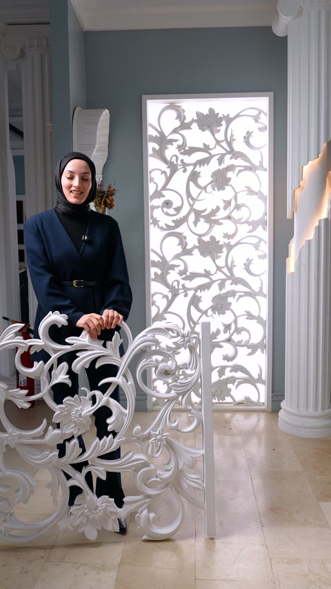 Sunucu, sütunlar arasındaki desenli uygulama önünde beyaz oyma parçayı sergiliyor