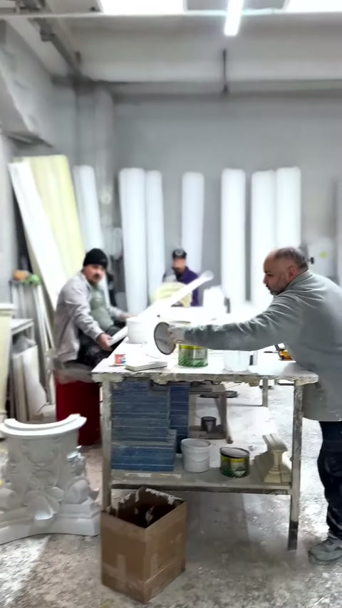 Usta, kaplar ve dekoratif elemanlarla dolu tezgahta çalışıyor.