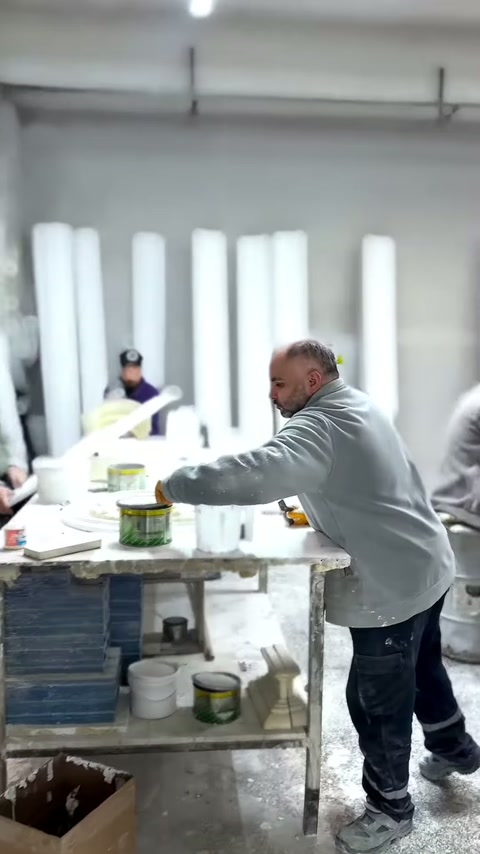 Gri önlüklü usta, beyaz süsleme parçasının yüzeyini işliyor.