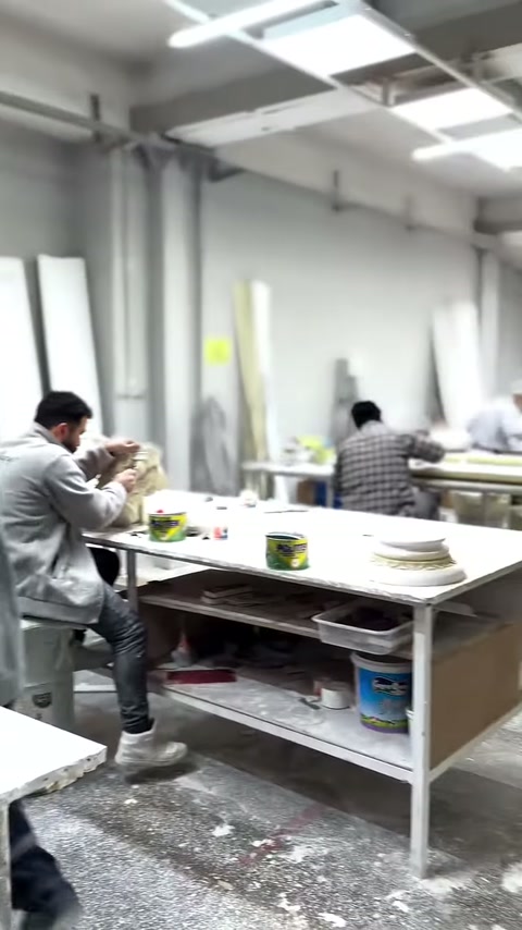 Çalışma alanında ustalar, uzun masalar üzerindeki dekoratif parçaları işliyor.