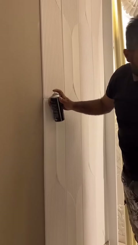 Beyaz duvar panelinin dikey kenarına son sprey uygulaması yapılıyor.