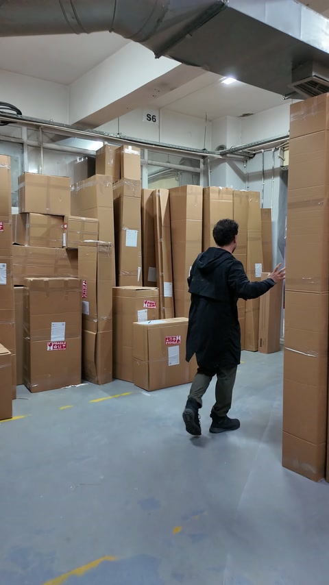 Usta, depo koridorundaki paketlenmiş ürün gruplarını işaret ediyor.