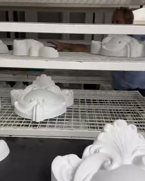 Üretim alanındaki raflarda sıralanmış çeşitli beyaz taç motifleri görülüyor
