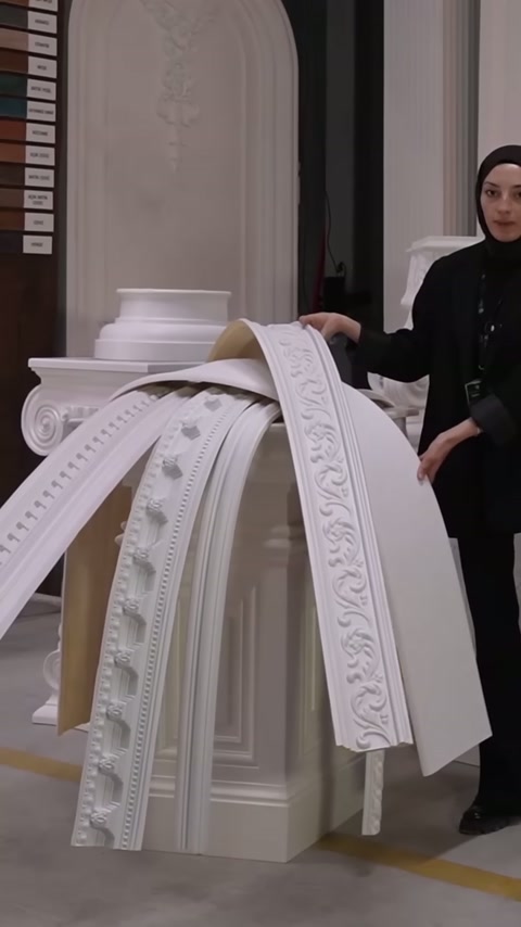 Beyaz düz panel, kıvrılmış dekoratif bordürlerin yanında dikey olarak sergileniyor
