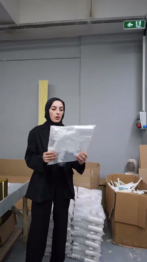 Sunucu, kare biçimli kabartmalı dekoratif parçayı elinde sergiliyor.