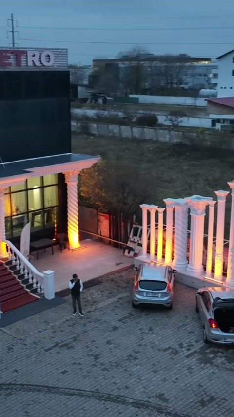 Farklı yükseklikteki beyaz kolonlar, giriş avlusunun yanında aydınlatılarak sıralanıyor