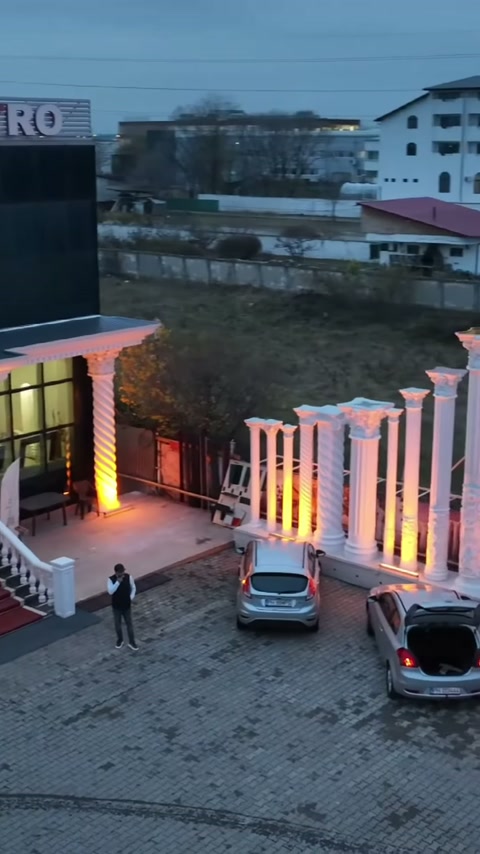 Sütunlu çevre duvarı, park edilmiş araçların arkasında cepheye bağlanıyor