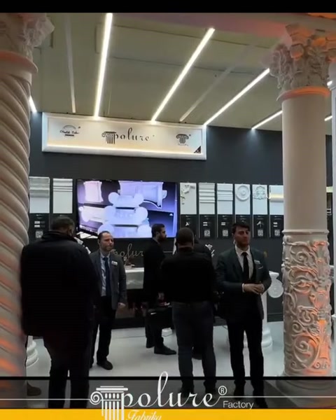 Sütunlu stand içinde ürün panoları ve ziyaretçiler yer alıyor