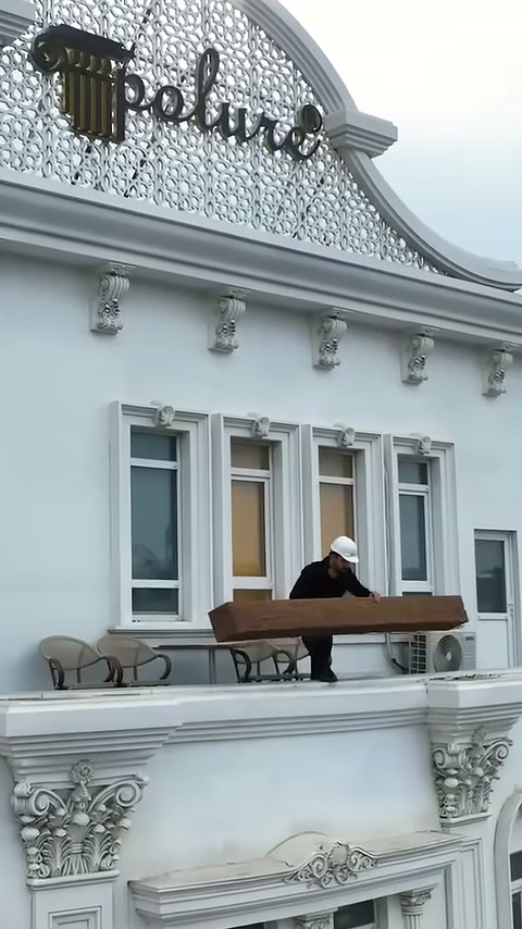 Usta üst kattaki terasta uzun ahşap dokulu kirişi hazırlıyor.