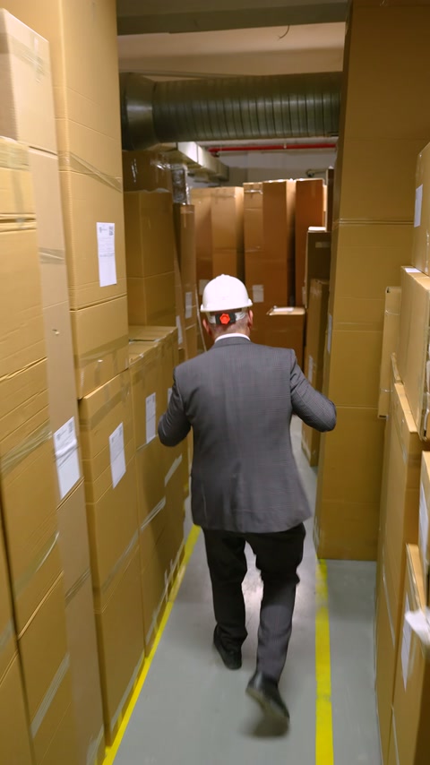 Baretli görevli paketlerin bulunduğu dar fabrika koridorunda duruyor.