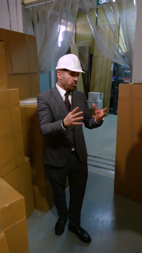 Görevli, yüksek ürün paketleri arasında teslimat kontrolünü açıklıyor.