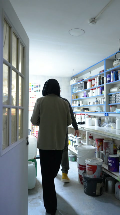 Laboratuvara giren ekip üyesi, raflı çalışma alanındaki görevliye yaklaşıyor