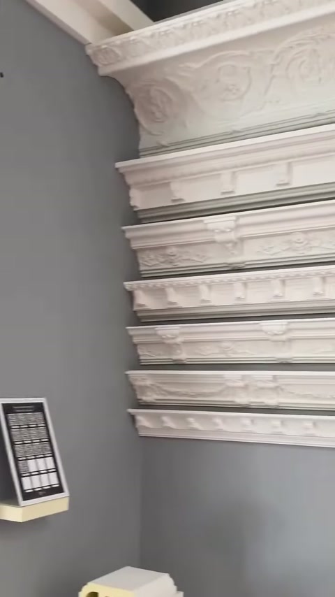 Gri duvarda çiçek bezemeli geniş kartonpiyer ve bordürler sıralanıyor.