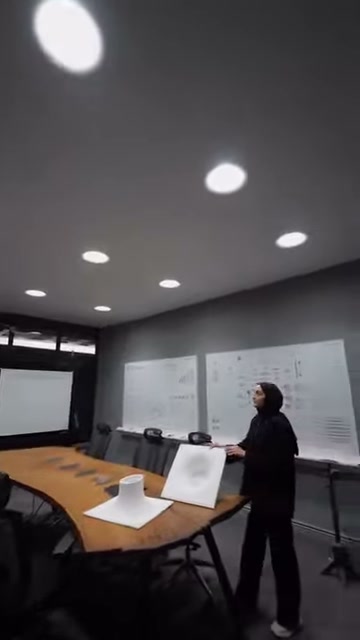 Sunucu toplantı alanındaki tavan aydınlatmasını eliyle işaret ediyor