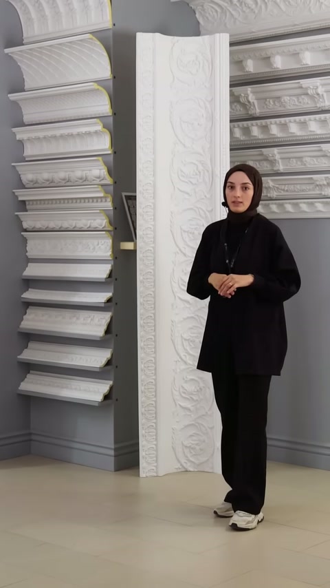 Showroomdaki sunucu, duvara dizilmiş kartonpiyer örneklerinin yanında duruyor.