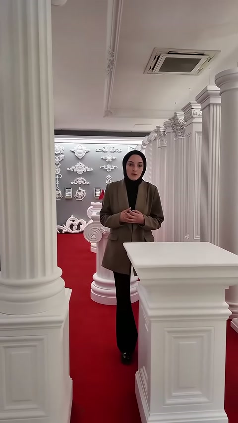 Sunucu beyaz sütun sıralarının arasında kameraya dönük duruyor