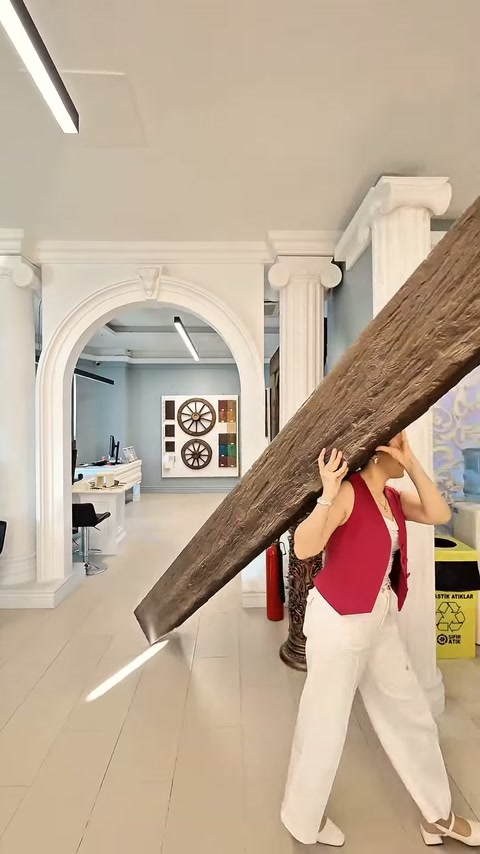 Kadın, ahşap desenli uzun kiriş parçasını vitrin alanından geçiriyor.