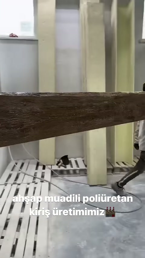 Çalışan tamamlanan kahverengi kirişi tezgâhtan kaldırarak taşıyor.