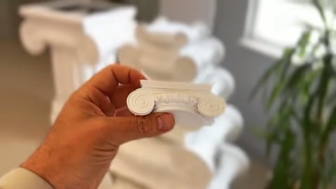 Kıvrımlı beyaz dekor parçası, sütun başlıklarının önünde sergileniyor.